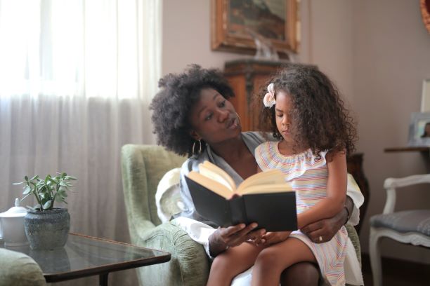 Black mother reading a book to biracial daughter in beautiful house