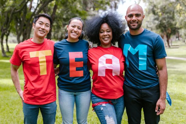 4 smiling people--Asian man, Latina or Indigenous woman, Black woman and Black, mixed or Arab man--stand in a row, wearing colorful shirts that spell out the word TEAM