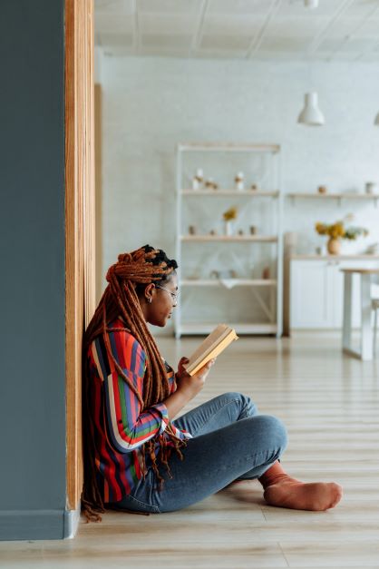 A woman in chunky box braids sitting on the floor while reading a book