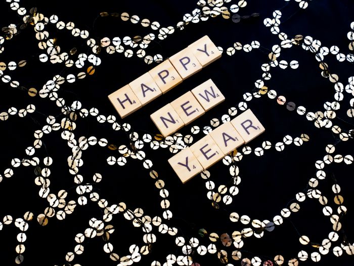 Scrabble tiles spell out Happy New Year on a black background dotted with sequins